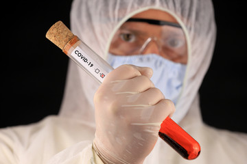 The doctor in a protective suit and mask holding a glass tube with a positive blood test result for...