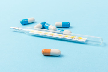 Pills isolated on blue background.Colorful medical drug capsule. Medical thermometer. Concept of coronavirus