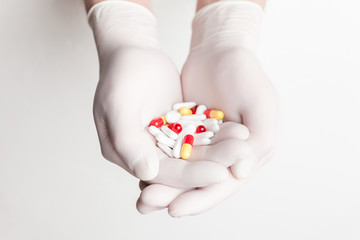 Colorful pills and tablets in doctor's hands in white medical gloves on white background.