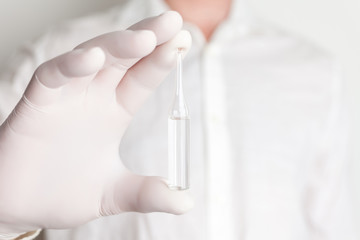 Ampoule with medicine in doctor's hand in white medical gloves on white background.