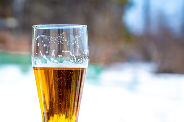 Light beer in a glass goblet on a picnic with snow background. Beer foam on the walls of a glass in the sunlight