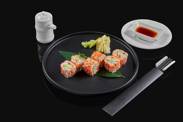 Appetizing sushi california roll with tobik caviar, crab, avocado and cucumber on a black ceramic plate on a black background. Japanese traditional food. Photo for the menu
