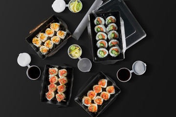 Obraz na płótnie Canvas Conceptual photo for sushi roll delivery. Rolls in cardboard packages on a black background. 3 types of spicy rolls with salmon, scallop and tuna, rolls with salmon and onions