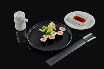 Traditional maki sushi rolls with salmon on a black plate in composition with soy sauce and chopsticks on a black background. Japanese food. Photo for the menu