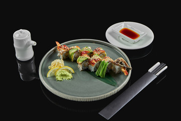Appetizing sushi rolls dragon with avocado, smoked eel and shrimp in a black ceramic plate with chopsticks and soy sauce. Black background. Traditional japanese food