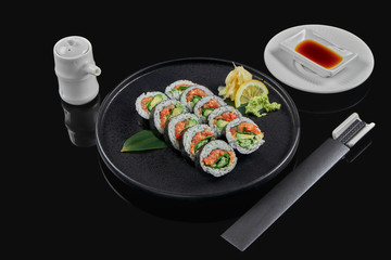 Sushi rolls with rice, nori, salmon, onions and cucumber on a black ceramic plate on a black background. Japanese traditional food. Sushi menu. Fuji roll