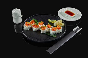 Spicy sushi rolls with rice, norms, mayonnaise, tobiko caviar and salmon on a black ceramic plate on a black background. Japanese traditional food.