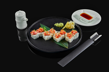 Spicy sushi rolls with rice, norms, mayonnaise, tobiko caviar and tuna on a black ceramic plate on a black background. Japanese traditional food.