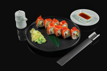 Classic Philadelphia roll with salmon, tobiko caviar, cream cheese and avocado on a stylish black plate on a black background. Traditional japanese food