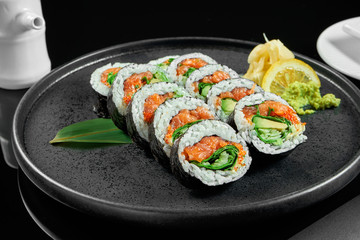 Sushi rolls with rice, nori, salmon, onions and cucumber on a black ceramic plate on a black background. Japanese traditional food. Sushi menu