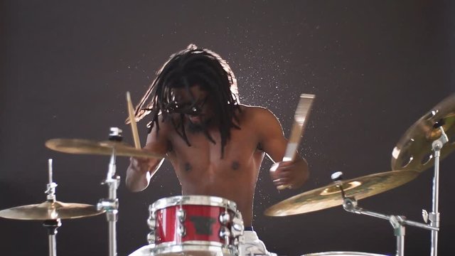 Professional african drummer man playing on drums and cymbals, wearing eyeglasses and holding sticks.