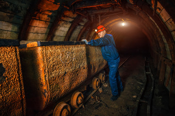 A miner in a coal mine stands near a trolley. Copy space.