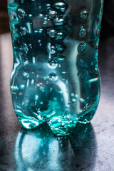 Movement of bubbles in carbonated soda soft drink in green plastic bottle on dark table, close up view 