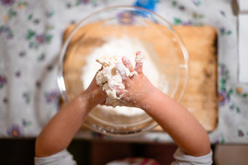 Closeup of the hands of a little girl while playing with pasta and flour in the kitchen during the quarantine from COVID-19