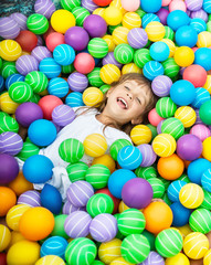 Fototapeta na wymiar Charming child lying in pool with bright multi-colored plastic balls. Girl dressed in pink blouse and white shorts