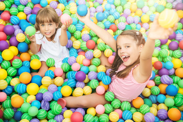 Fototapeta na wymiar Cheerful children smiling and playing in playroom with plastic balls. Hands raised up and holding toys