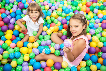 Fototapeta na wymiar Two girls playing in pool with colorful plastic balls in game room. Child looking at camera