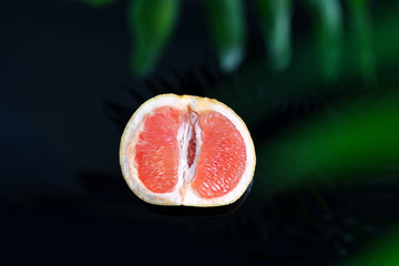 Half of fresh ripe grapefruit against a blurred natural background with green palm leaf.