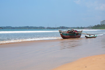 A multi-colored with fishing nets a boat stands on the shore of the Indian Ocean on the background of the island of Sri Lanka