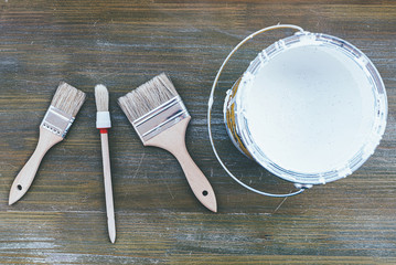 top view of different paint brushes and white paint on wooden surface, home improvement concept