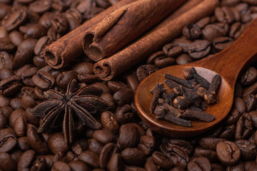 Sticks of cinnamon, anise and cloves in a wooden spoon against the background of coffee beans
