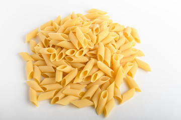 Heap of dried mezze penne rigate Italian pasta ready to be cooked, isolated on a white table, top view or flat lay of healthy food 
