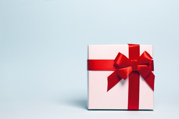 Present box  wrapped with red ribbon on pastel background.