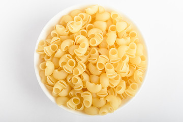 Dried cornetti rigati Italian pasta in a round bowl ready to be cooked, isolated on a white table, top view or flat lay of healthy food 
