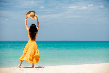 Happy  traveler  asian woman  in dress standing on the beach  holding sun hat  enjoys  her  tropical  vacation