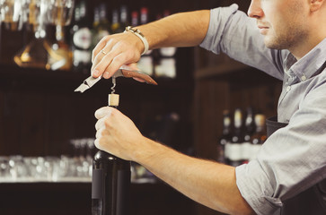 Bartender concentrated on uncork of elite drink at bar counter.