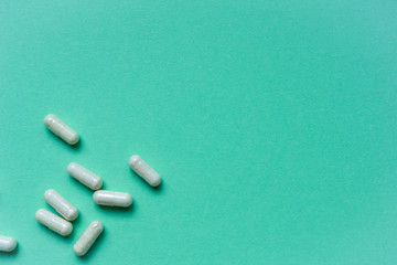 Top view of bunch of pills in bottom left corner on green background. Concept of first aid, medical care during illness. Flat lay. Space for text.