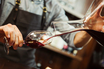 Sommelier pouring wine into glass from mixing bowl. Male waiter