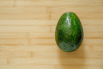 Whole avocado on the right on a wooden table, close up, top view