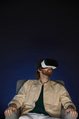 Fototapeta na wymiar Vertical portrait of modern bearded man wearing virtual reality gear while enjoying immersive videogame or movie in dark, copy space