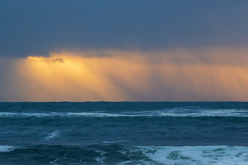 Obraz premium A rainstorm over the ocean with beautiful orange sky 