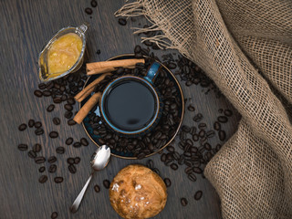 cup of coffee with cinnamon sticks, orange jam, bun and canvas on brown table