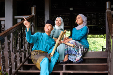 A group of malay muslim people in traditional costume having happy conversation during Aidilfitri celebration at terrace of traditional wooden house