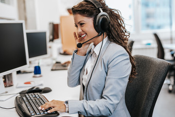 Portrait of beautiful smiling female call-center agent with headset working on support in the...