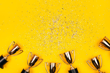 Golden winner cups with silver sparkles on a yellow background with copy space. Festive concept....