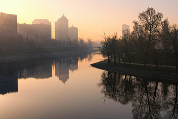 Picturesque morning city landscape. Rusanivka canal with embankment and silhouettes of old multi-story houses. They reflected in the blue water. Little haze during sunrise. Rusanivka, Kyiv, Ukraine