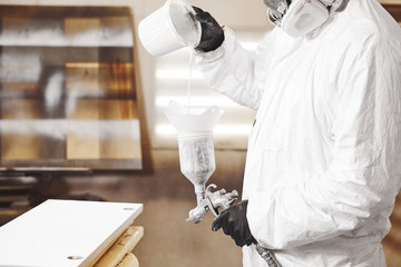 Obraz premium Man pours paint into the sprayer before painting the wood.