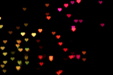 Fototapeta na wymiar Blurred view of heart shaped lights on black background. Bokeh effect