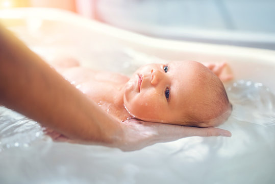 Small cute big-eyed beautiful baby bathes in warm water in the hands of a caring mother. The concept of baby care and child care
