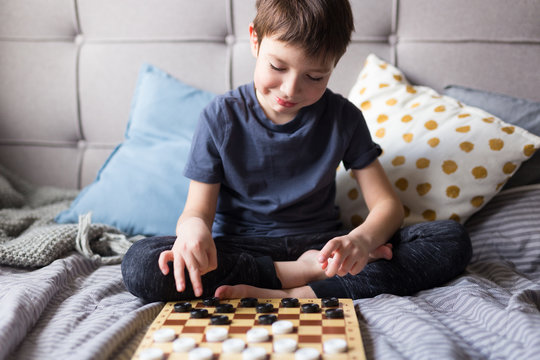 Young Kid Hands Playing Checkers Table Game On Bed. Stay At Home Quarantine Concept. Board Game And Kids Leisure Concept. Family Time. 