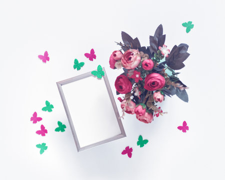 A metal photo frame and a bouquet of flowers are on a white background. Nearby are figures of butterflies made of felt. Minimalist arrangement. Flat lay. Copy space.