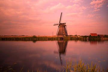 Fototapeta na wymiar A windmill by a canal in Kinderdijk Holland is reflected in the water.