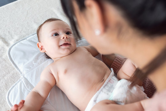 Smiling baby is having fun with her mother while changing his diaper at home.