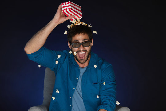 Portrait of joyful bearded man wearing 3D glasses throwing popcorn over head while watching movie at home in dark, copy space
