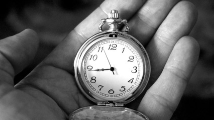 Old antique pocket watch showing time being held in hand. Close up black and white photography