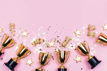 Winner cups with confetti and festive stars on a pastel background with copy space on top. Flat lay style.